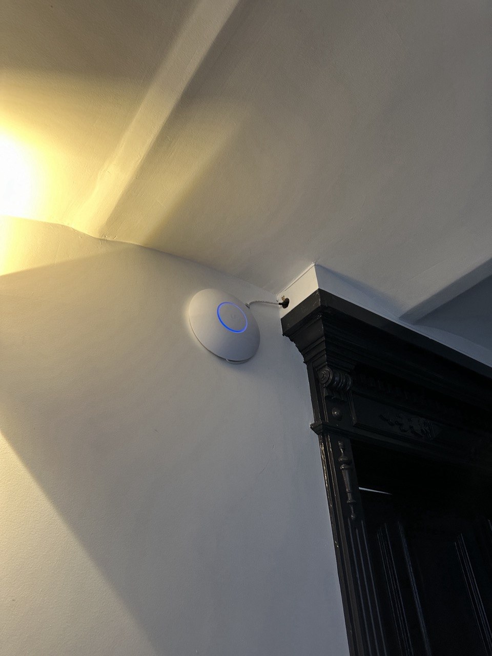 An der Wand montierter UniFi Access Point neben einer dunklen Tür
